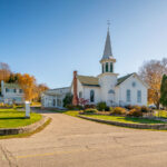 The Ephraim Moravian Church, located in the heart of Ephraim, Wisconsin, dates back to the mid-19th century and reflects the town’s deep Moravian heritage. Founded in 1853 by Norwegian settlers under the leadership of Reverend Andreas Iverson, the congregation built this white clapboard church overlooking Eagle Harbor as both a house of worship and a symbol of unity for the early Door County community. The building’s steeple, traditional in form yet understated in design, continues to define Ephraim’s skyline, linking the village’s modern charm with its Scandinavian and religious roots.