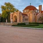Warm evening light falls on the Lakewood Memorial Chapel in Minneapolis, its pink granite walls and red-tiled domes glowing against the autumn trees. Built in 1910, the chapel blends Byzantine and Romanesque styles, standing as one of the city’s most architecturally significant landmarks.
