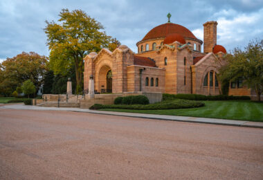 Warm evening light falls on the Lakewood Memorial Chapel in Minneapolis, its pink granite walls and red-tiled domes glowing against the autumn trees. Built in 1910, the chapel blends Byzantine and Romanesque styles, standing as one of the city’s most architecturally significant landmarks.