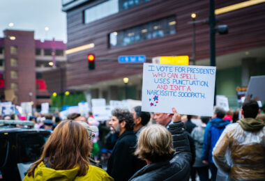 Man holds up a sign that reads "I vote for presidents who can spell, uses punctuation and isn't a narcissistic sociopath." outside the Target Center during a Trump protest on October 10, 2019.