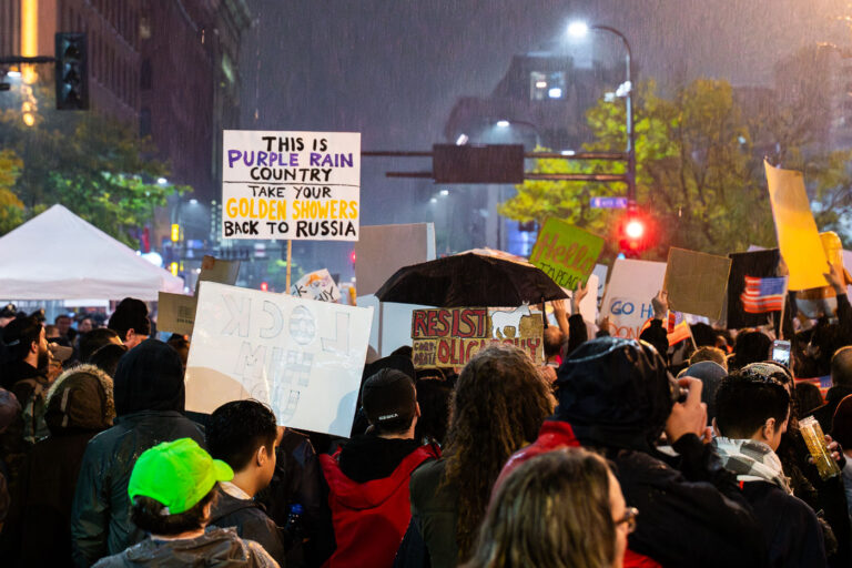 Protesters Gather Outside Trump Rally in Downtown Minneapolis, 2 4 Protesters fill the intersection near the Target Center in downtown Minneapolis during Donald Trump’s campaign rally on October 10, 2019. Demonstrators carried homemade signs, including one reading “This is Purple Rain Country—Take Your Golden Showers Back to Russia,” referencing Minnesota’s musical icon Prince and the controversies surrounding Trump’s presidency. The rally drew thousands of protesters and supporters alike, marking one of the city’s largest political demonstrations since the 2016 election.