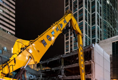 A Royal Taylor demolition excavator works overnight in downtown Chicago, dismantling the remains of a mid-century parking structure near North Wabash Avenue. The location, part of an area undergoing major redevelopment, reflects the city’s continual cycle of teardown and renewal. Once a dense cluster of low-rise commercial and industrial buildings, this district is being transformed by modern high-rise towers and mixed-use developments that are reshaping the skyline and urban streetscape of central Chicago.