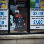 Trump Supporter at Downtown Bar Before Rally 3 A woman wearing a “Trump 2020” hat smiles from inside a downtown Minneapolis bar near the Target Center on October 10, 2019. The establishment, decorated with promotional posters for discounted beer and wings, became a temporary gathering spot for attendees arriving early to the president’s evening campaign rally. The 2019 visit marked a rare appearance by a sitting U.S. president in Minneapolis and drew both supporters and demonstrators into the city’s entertainment district, where security and anticipation heightened throughout the afternoon.