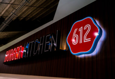 An illuminated “612 Burger Kitchen” sign inside U.S. Bank Stadium in Minneapolis, named after the city’s area code. The bold red-and-black typography and retro badge design reflect a blend of local identity and modern stadium branding. Located among the venue’s food and beverage concessions, 612 Burger Kitchen is part of the stadium’s effort to feature Minneapolis-based culinary offerings for fans attending Minnesota Vikings games and large-scale events.
