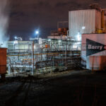 Steam rises from the Barry & Sewall Chemical Company complex in Northeast Minneapolis, a facility known for producing adhesives, coatings, and specialty chemicals for over a century. Illuminated by floodlights and framed by dense pipe networks, the site reflects the city’s enduring industrial infrastructure along the rail and river corridors. The hand-painted logo on the wall remains a remnant of mid-20th-century branding still visible across many older manufacturing sites in the Twin Cities.