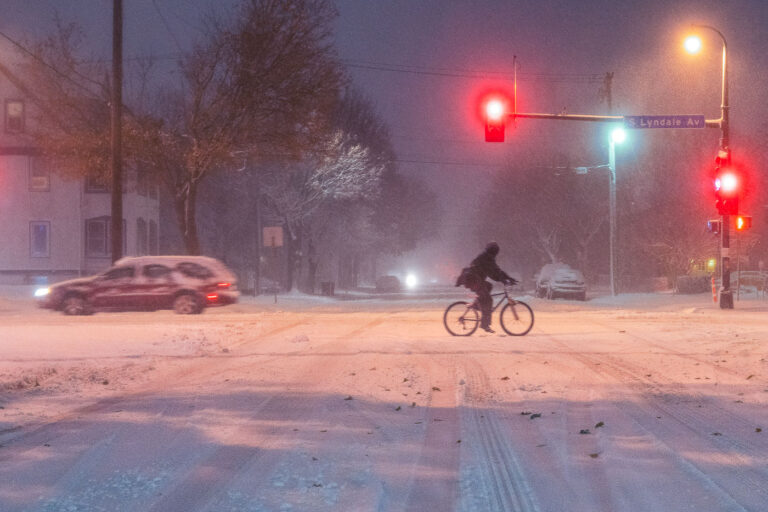 Cyclist on Lyndale Avenue During 2019 Snowstorm 4 A cyclist crosses Lyndale Avenue South during the heavy November 26, 2019 snowstorm in Minneapolis. Despite low visibility and slick streets, a few commuters still braved the conditions, illuminated by red traffic lights and snow-diffused streetlamps. The image captures the perseverance of winter cycling culture in the Twin Cities, where even severe weather rarely stops movement through the urban grid.