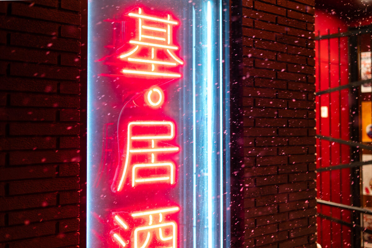Moto-i neon sign in snow on Lyndale Avenue in Minneapolis, lit against a brick wall.