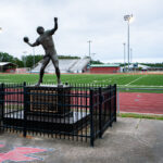 In Kiln, Mississippi, the legacy of Brett Favre looms large. Outside Hancock High School’s football stadium, a life-sized statue of the quarterback stands mid-throw, immortalizing the local athlete who went on to become one of the NFL’s most prolific passers. Set against the backdrop of the school’s red track and green turf, the monument reflects both community pride and the enduring place of football in Southern culture. For locals, it serves as a reminder that even from a small Gulf Coast town, greatness can reach the national stage.