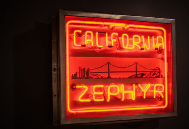 This neon sign once promoted the California Zephyr, one of the most celebrated passenger trains of the postwar era. First introduced in 1949, the train linked Chicago to the San Francisco Bay Area, offering panoramic views of the Rockies and the Sierra Nevada. The glowing red lettering, paired with imagery of a bridge, skyline, and streamlined locomotive, reflects the optimism of mid-20th-century American rail travel and the romance of crossing the continent in comfort and style.