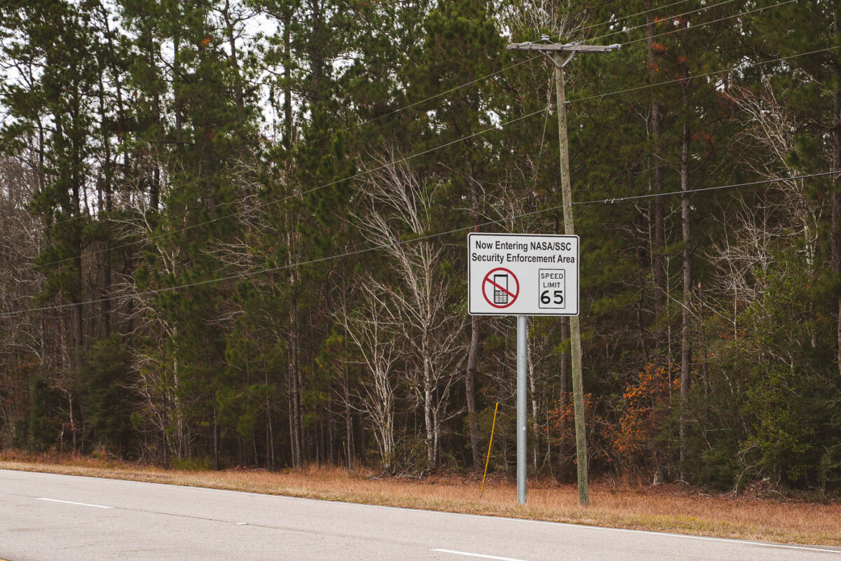 Along a quiet stretch of pine-lined Highway 607 in Hancock County, Mississippi, a sign alerts motorists: Now Entering NASA/SSC Security Enforcement Area. Beyond this point lies the vast Stennis Space Center, where engines for Apollo, the Space Shuttle, and Artemis have been tested at full throttle. The reminder of security restrictions — paired with the speed limit notice — reflects how an otherwise ordinary southern highway doubles as the gateway to one of the most advanced propulsion test facilities in the world.