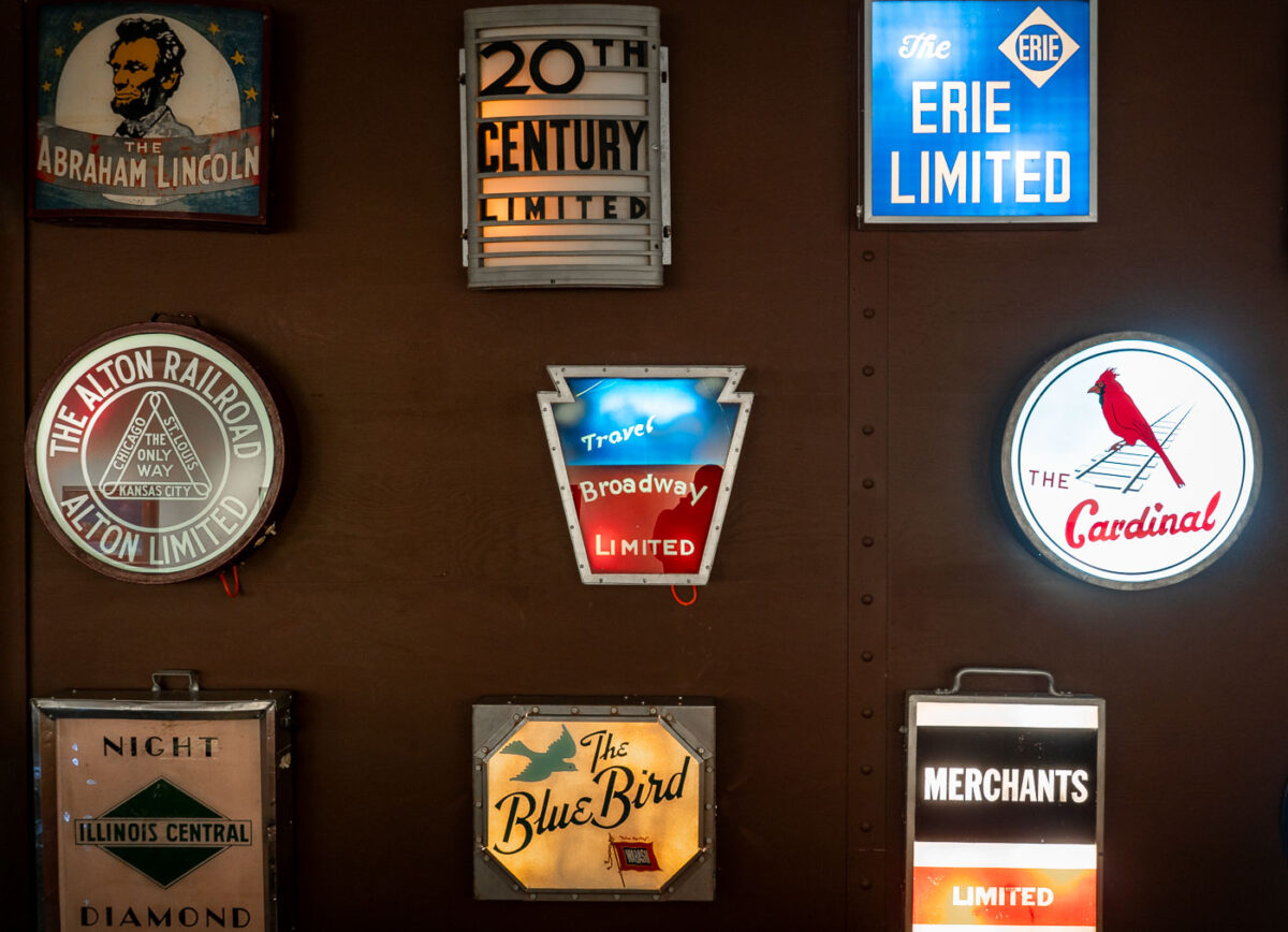Seen inside the Green Bay Railroad Museum, an exhibit of historic railroad drumhead signs, once mounted on the observation cars of famous American passenger trains. These illuminated signs served both as branding and a wayfinding tool for travelers during the golden age of rail.


	• 20th Century Limited – The legendary New York Central luxury express between New York and Chicago, famous for its red carpet treatment.
	• Broadway Limited – The Pennsylvania Railroad’s flagship train, symbolized by its keystone-shaped sign.
	•	The Cardinal – Still in operation today as an Amtrak route between New York and Chicago via Washington, D.C. and Cincinnati.
	•	The Abraham Lincoln – Operated by the Alton Railroad between Chicago and St. Louis.
	•	The Blue Bird – Another Alton Railroad streamliner that connected Chicago and St. Louis.
	•	Erie Limited – A long-distance train operated by the Erie Railroad.
	•	Night Diamond (Illinois Central) – A named overnight passenger service.
	•	Merchants Limited – A New Haven Railroad luxury train between Boston and New York, a favorite among business travelers.

	•	20th Century Limited – The legendary New York Central luxury express between New York and Chicago, famous for its red carpet treatment.
	•	Broadway Limited – The Pennsylvania Railroad’s flagship train, symbolized by its keystone-shaped sign.
	•	The Cardinal – Still in operation today as an Amtrak route between New York and Chicago via Washington, D.C. and Cincinnati.
	•	The Abraham Lincoln – Operated by the Alton Railroad between Chicago and St. Louis.
	•	The Blue Bird – Another Alton Railroad streamliner that connected Chicago and St. Louis.
	•	Erie Limited – A long-distance train operated by the Erie Railroad.
	•	Night Diamond (Illinois Central) – A named overnight passenger service.
	•	Merchants Limited – A New Haven Railroad luxury train between Boston and New York, a favorite among business travelers.