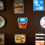 Seen inside the Green Bay Railroad Museum, an exhibit of historic railroad drumhead signs, once mounted on the observation cars of famous American passenger trains. These illuminated signs served both as branding and a wayfinding tool for travelers during the golden age of rail.	• 20th Century Limited – The legendary New York Central luxury express between New York and Chicago, famous for its red carpet treatment.	• Broadway Limited – The Pennsylvania Railroad’s flagship train, symbolized by its keystone-shaped sign.	•	The Cardinal – Still in operation today as an Amtrak route between New York and Chicago via Washington, D.C. and Cincinnati.	•	The Abraham Lincoln – Operated by the Alton Railroad between Chicago and St. Louis.	•	The Blue Bird – Another Alton Railroad streamliner that connected Chicago and St. Louis.	•	Erie Limited – A long-distance train operated by the Erie Railroad.	•	Night Diamond (Illinois Central) – A named overnight passenger service.	•	Merchants Limited – A New Haven Railroad luxury train between Boston and New York, a favorite among business travelers.	•	20th Century Limited – The legendary New York Central luxury express between New York and Chicago, famous for its red carpet treatment.	•	Broadway Limited – The Pennsylvania Railroad’s flagship train, symbolized by its keystone-shaped sign.	•	The Cardinal – Still in operation today as an Amtrak route between New York and Chicago via Washington, D.C. and Cincinnati.	•	The Abraham Lincoln – Operated by the Alton Railroad between Chicago and St. Louis.	•	The Blue Bird – Another Alton Railroad streamliner that connected Chicago and St. Louis.	•	Erie Limited – A long-distance train operated by the Erie Railroad.	•	Night Diamond (Illinois Central) – A named overnight passenger service.	•	Merchants Limited – A New Haven Railroad luxury train between Boston and New York, a favorite among business travelers.