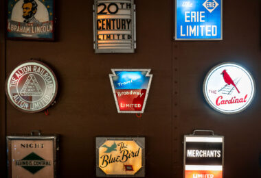 Seen inside the Green Bay Railroad Museum, an exhibit of historic railroad drumhead signs, once mounted on the observation cars of famous American passenger trains. These illuminated signs served both as branding and a wayfinding tool for travelers during the golden age of rail.


	• 20th Century Limited – The legendary New York Central luxury express between New York and Chicago, famous for its red carpet treatment.
	• Broadway Limited – The Pennsylvania Railroad’s flagship train, symbolized by its keystone-shaped sign.
	•	The Cardinal – Still in operation today as an Amtrak route between New York and Chicago via Washington, D.C. and Cincinnati.
	•	The Abraham Lincoln – Operated by the Alton Railroad between Chicago and St. Louis.
	•	The Blue Bird – Another Alton Railroad streamliner that connected Chicago and St. Louis.
	•	Erie Limited – A long-distance train operated by the Erie Railroad.
	•	Night Diamond (Illinois Central) – A named overnight passenger service.
	•	Merchants Limited – A New Haven Railroad luxury train between Boston and New York, a favorite among business travelers.

	•	20th Century Limited – The legendary New York Central luxury express between New York and Chicago, famous for its red carpet treatment.
	•	Broadway Limited – The Pennsylvania Railroad’s flagship train, symbolized by its keystone-shaped sign.
	•	The Cardinal – Still in operation today as an Amtrak route between New York and Chicago via Washington, D.C. and Cincinnati.
	•	The Abraham Lincoln – Operated by the Alton Railroad between Chicago and St. Louis.
	•	The Blue Bird – Another Alton Railroad streamliner that connected Chicago and St. Louis.
	•	Erie Limited – A long-distance train operated by the Erie Railroad.
	•	Night Diamond (Illinois Central) – A named overnight passenger service.
	•	Merchants Limited – A New Haven Railroad luxury train between Boston and New York, a favorite among business travelers.