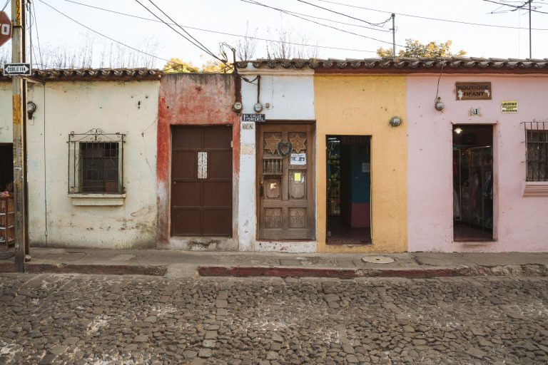 Row of Storefronts on 1a Calle Poniente, Antigua 2 Row of colorful single-story colonial buildings with wooden doors lines a cobblestone street in Antigua Guatemala.