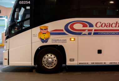 A Coach USA intercity bus displaying the Megabus “$1 fare” mascot along its passenger side, indicating that the service accepts Megabus.com tickets. Coach USA, a subsidiary of Stagecoach Group, operates regional and interstate routes across the United States, often in partnership with Megabus since their brands share booking systems and fleet resources. The bus shown is an MCI J4500 model, widely used for long-distance motorcoach travel due to its capacity and highway comfort. The collaboration between Megabus and Coach USA expanded low-cost express travel options throughout the Midwest and beyond, allowing travelers to board Coach USA-operated vehicles with tickets purchased via Megabus’s digital platform.