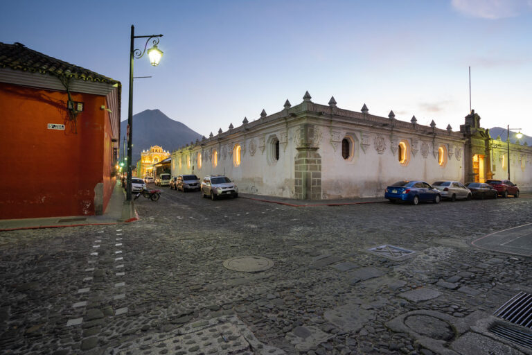Antigua Guatemala: 5a Calle Oriente and Agua Volcano at Dusk 3 5a Calle Oriente in Antigua, Guatemala, is a historic street paved with cobblestones, a common feature in colonial-era cities. The street is illuminated by traditional lampposts, casting a warm glow on the surrounding architecture as dusk settles. In the background, the Agua Volcano, a stratovolcano that has been dormant since 1906, looms over the city. Antigua Guatemala itself served as the Spanish colonial capital of Central America from 1543 until 1773, when earthquakes destroyed much of the city, leading to the capital's relocation to present-day Guatemala City.