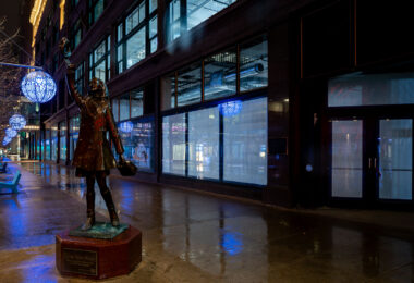 The iconic bronze statue of Mary Tyler Moore along Nicollet Mall in downtown Minneapolis, depicting the memorable hat-tossing moment from the opening of The Mary Tyler Moore Show, which first aired in 1970 and helped cement Minneapolis in television history. Installed in 2002, the statue symbolizes the city’s cultural association with the show’s themes of independence and optimism. At the time of this photograph, Nicollet Mall—normally a busy pedestrian and transit corridor—appears unusually empty, reflecting the early days of COVID-19 shutdowns that drastically reduced public presence in city centers. Blue public art lanterns, added during street improvements completed in 2017, line the renovated streetscape, emphasizing Nicollet Mall’s evolution as both a commercial and cultural landmark.