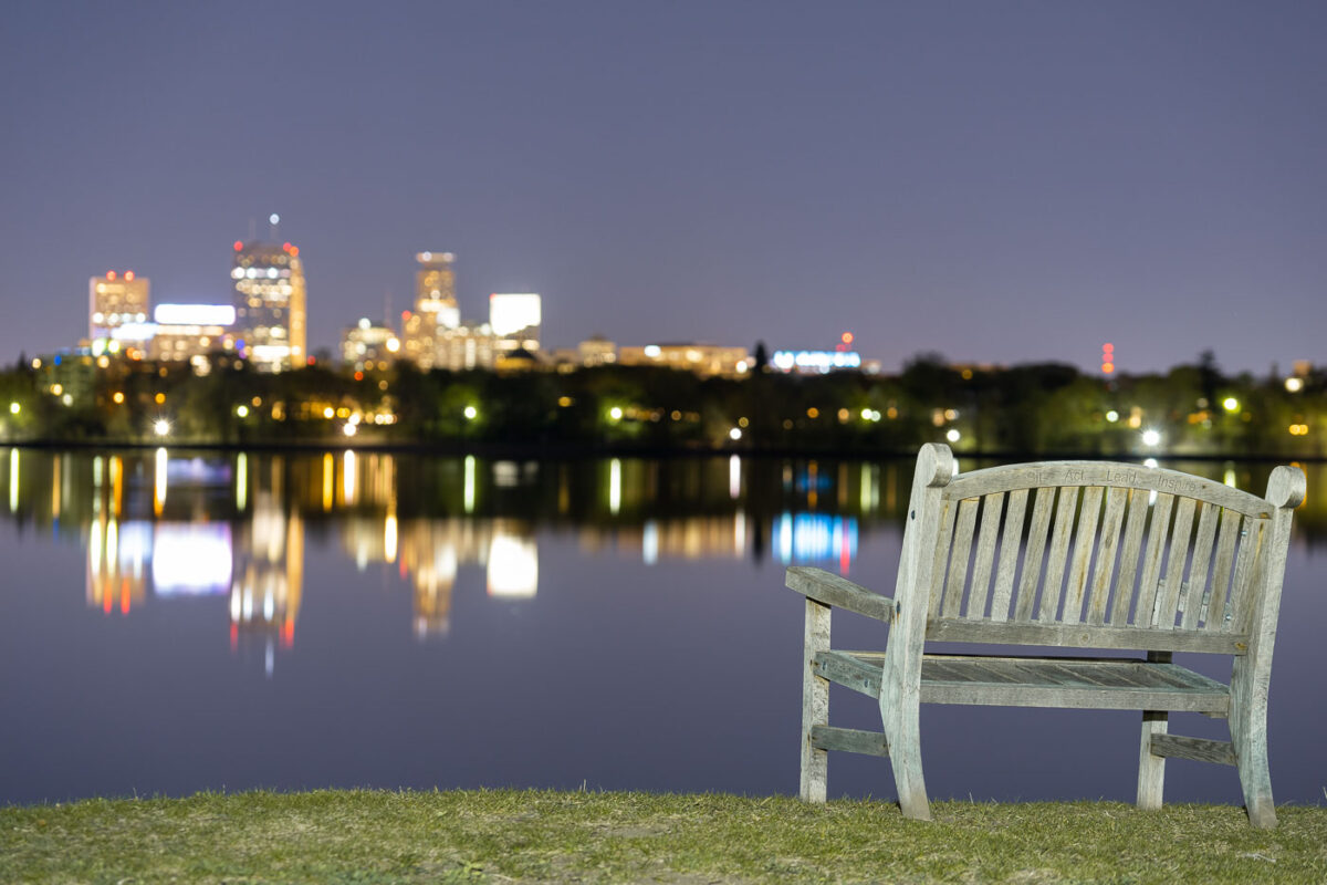 A bench at Bde Maka Ska in South Minneapolis. The Minneapolis skyline seen across the lake.