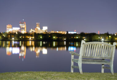 A bench at Bde Maka Ska in South Minneapolis. The Minneapolis skyline seen across the lake.