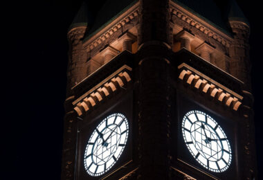 The clock tower of Minneapolis City Hall glows at night, its illuminated faces visible across downtown. The landmark’s Romanesque architecture remains a defining feature of the city’s skyline.