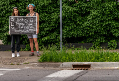 A couple hold up a sign that reads “Justice for George Floyd” on 36th St while others began to gather at the intersection of 38th St and Chicago Ave where Floyd was killed the night before.