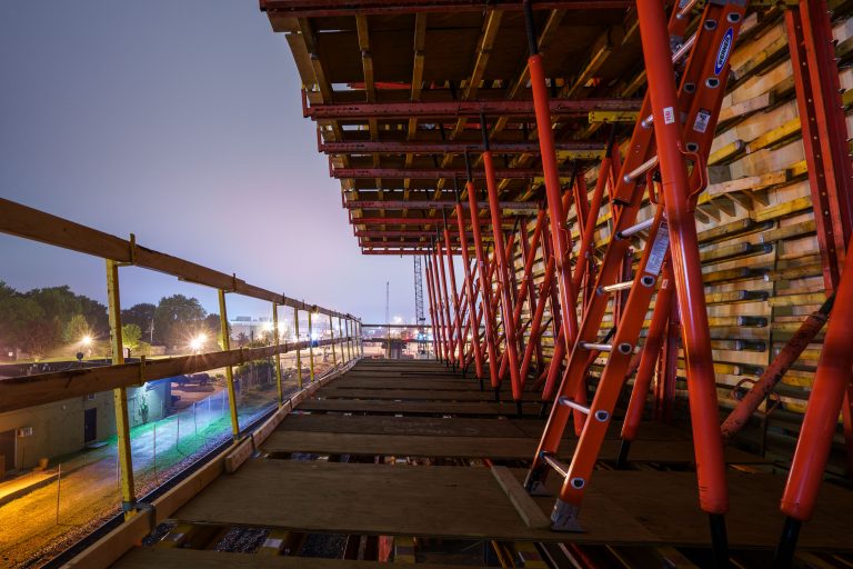 Red steel bridge structure under construction over Excelsior Boulevard in St. Louis Park at dusk.