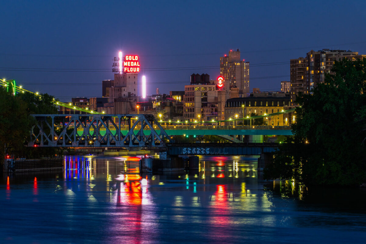 Downtown Minneapolis as seen from Boom Island in May 2020. Gold Medal Flour and Northstar Blankets neon signs visible across the Mississippi River.