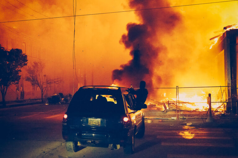 Car drives by a burning apartment building 3 A 6-story new housing development on fire near the Minneapolis Police 3rd Precinct during the 2nd day of protests in Minneapolis following the death of George Floyd.