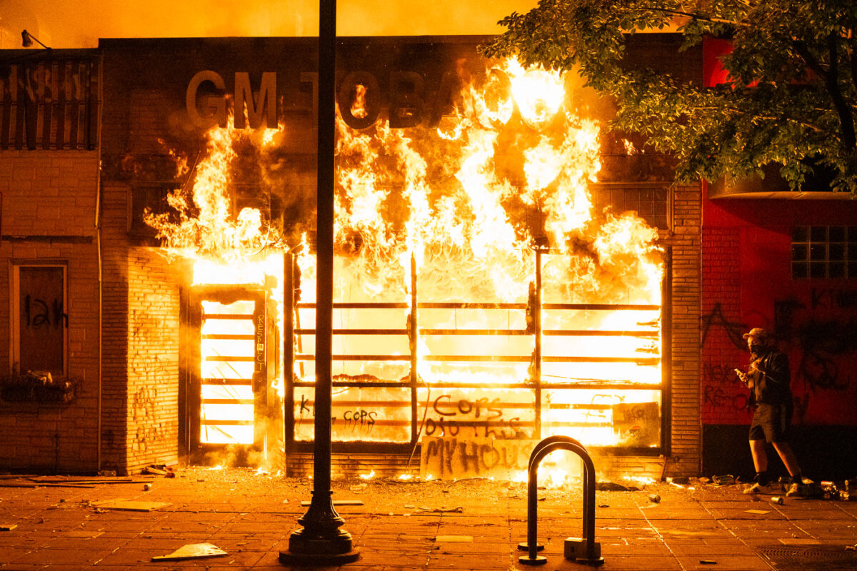 GM Tobacco, a block away from the Minneapolis Police 3rd Precinct, on fire as a protester walks by.