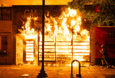 GM Tobacco, a block away from the Minneapolis Police 3rd Precinct, on fire as a protester walks by.