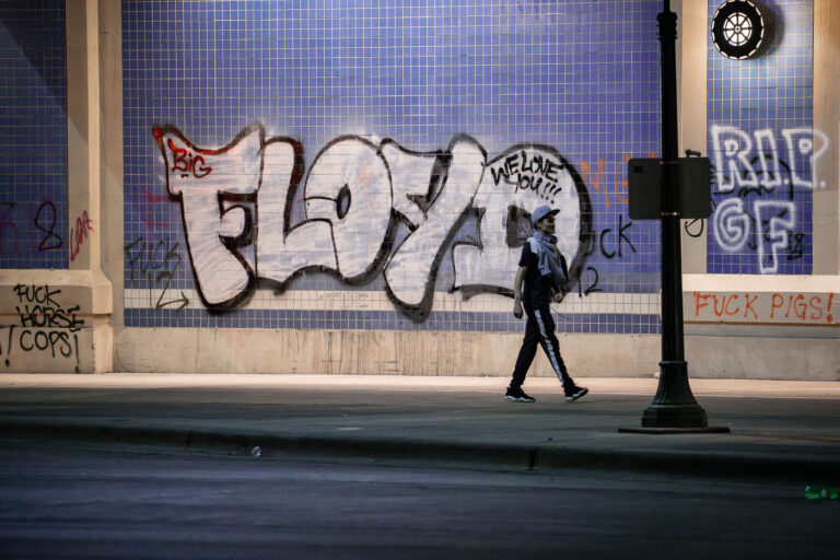 Protester walks past "FLOYD" on Lake Street 1 A protester waked under Haiwatha Ave where “FLOYD” is written on the wall. This on the 2nd day of protests in Minneapolis following the death of George Floyd.