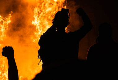 Protesters hold up their firsts while the Minneapolis Police 3rd Precinct burns in the background on May 28, 2020.