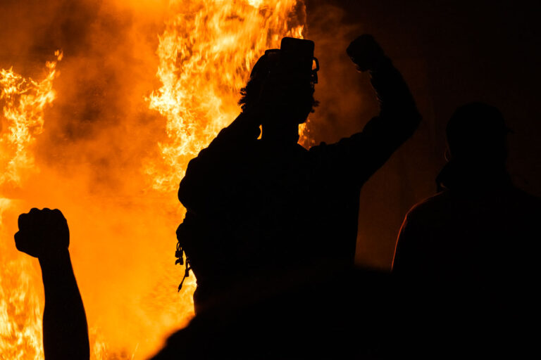 Protester in front of burning Minneapolis police station 1 Protesters hold up their firsts while the Minneapolis Police 3rd Precinct burns in the background on May 28, 2020.