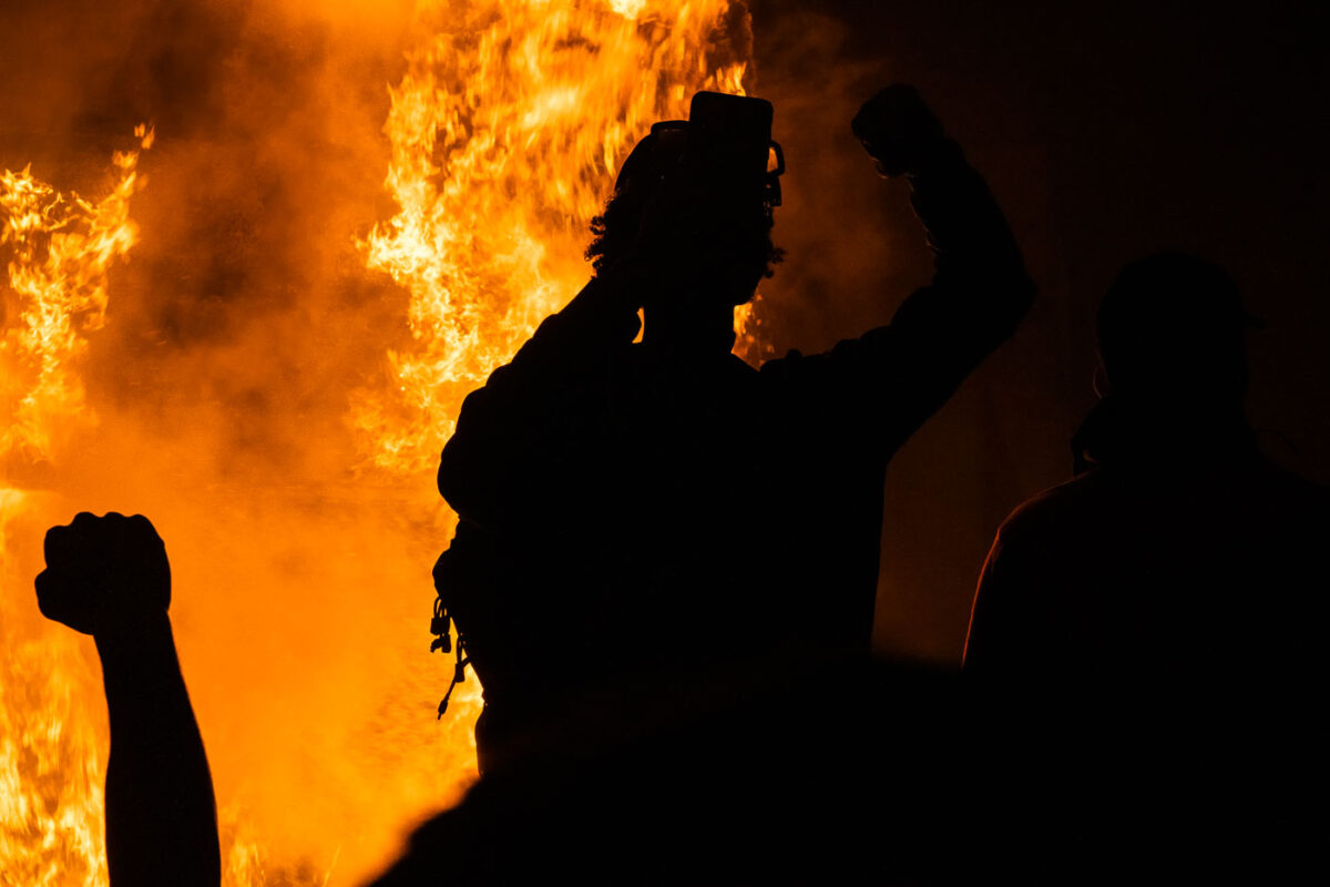 Protesters hold up their firsts while the Minneapolis Police 3rd Precinct burns in the background on May 28, 2020.