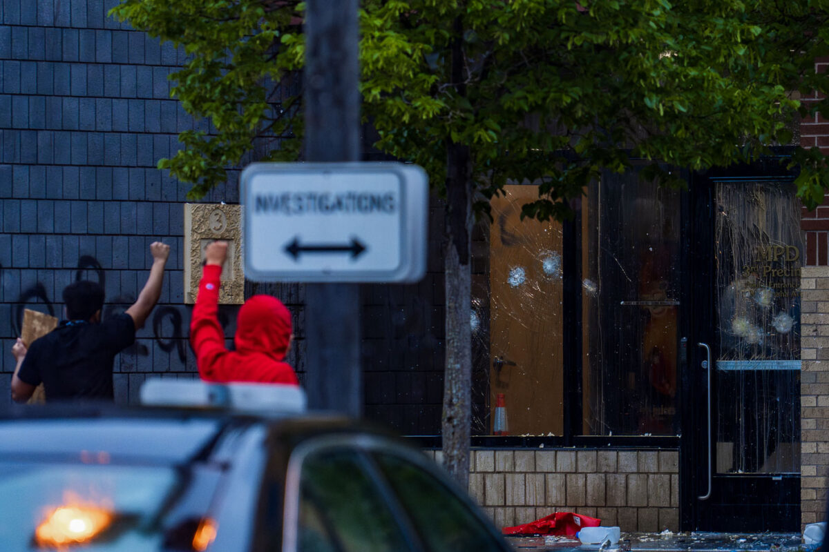 Protesters hold their fists up outside the Minneapolis Police 3rd Precinct police station. Police officers behind broken glass on day 1 of protests after the death of George Floyd the night before.