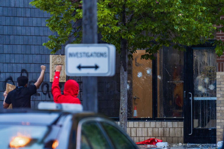 Raised fist at the Minneapolis Police 3rd Precinct 4 Protesters hold their fists up outside the Minneapolis Police 3rd Precinct police station. Police officers behind broken glass on day 1 of protests after the death of George Floyd the night before.