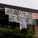 A sign reading "White supremacy is a public health crisis. We.Are.The.Cure. Anti-Racism NOW" hanging over the side of the Minneapolis Police Third Precinct on May 31, 2020.