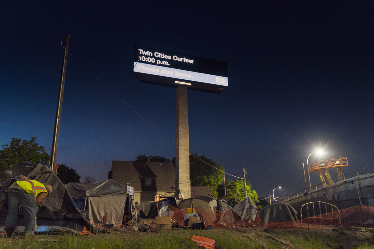Billboard reading "Twin Cities Curfew. Please stay home" with a homeless camp below. Shot during the 2020 Minneapolis unrest over the May 25th death of George Floyd.