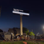 Billboard reading "Twin Cities Curfew. Please stay home" with a homeless camp below. Shot during the 2020 Minneapolis unrest over the May 25th death of George Floyd.