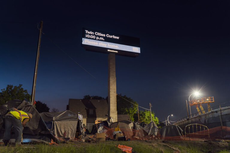 Encampment below billboard 1 Billboard reading "Twin Cities Curfew. Please stay home" with a homeless camp below. Shot during the 2020 Minneapolis unrest over the May 25th death of George Floyd.