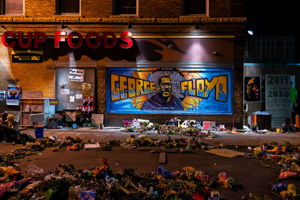 A large George Floyd mural on 38th Street with flowers left behind in front of it. George Floyd was killed around the corner on Chicago Ave the month prior.