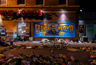 A large George Floyd mural on 38th Street with flowers left behind in front of it. George Floyd was killed around the corner on Chicago Ave the month prior.