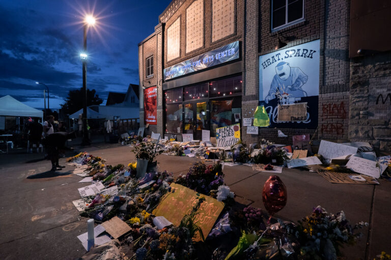 George Floyd Memorial, 38th & Chicago Ave, Minneapolis 4 Offerings of flowers, signs, and candles line the sidewalk at the George Floyd Memorial, located at 38th Street and Chicago Avenue in Minneapolis. These tributes were placed approximately one week after George Floyd was killed by police on May 25, 2020, transforming the site into a spontaneous public memorial. The area, now widely known as George Floyd Square, became a central gathering point for protests against racial injustice and police brutality. It continues to serve as a significant site for remembrance, community activism, and ongoing calls for systemic change.