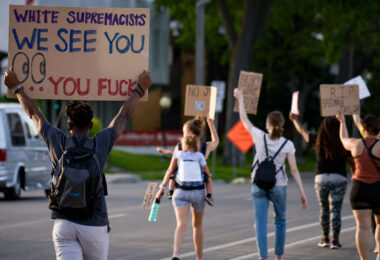 Protester holds up a sign reading “White supremacists We See You… you fucks” as they march down Park Avenue into downtown Minneapolis.