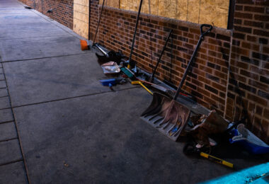 Brooms and shovels on the side of a building for community cleanup of damaged buildings during civil unrest in Minneapolis.
