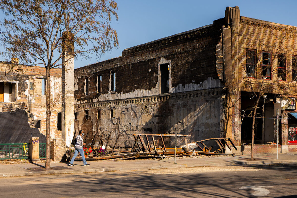 Woman walking in front of the remains of Chicago Furniture. The store was burned during unrest in Minneapolis following the May 25th, 2020 death of George Floyd.