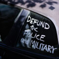 A car with “Defund the police and military” written on a window.