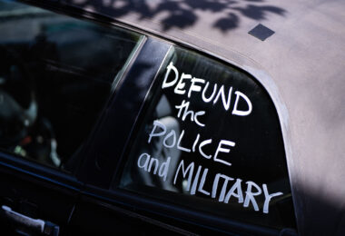 A car with “Defund the police and military” written on a window.
