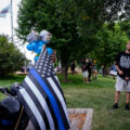 Man stands with a large gun with Black Lives Matters protesters behind him at a  "Back The Blue" rally in Woodbury, Minnesota on August 8th, 2020.