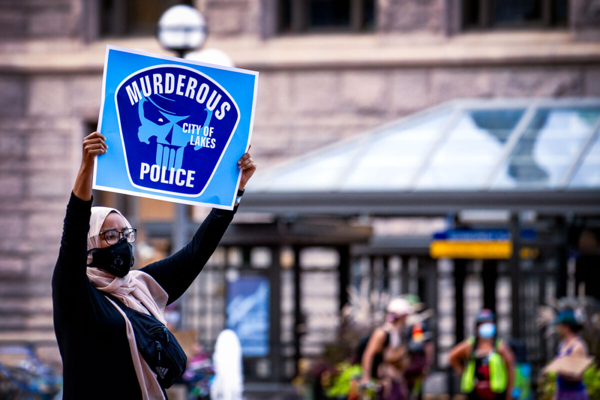 Woman holds up a sign that reads "Murderous Police" "City Of Lakes" at a protest and march in solidarity for Jacob Blake held in downtown Minneapolis at the Hennepin County Government Center.